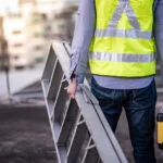 Man carrying ladder in high vis jacket representing importance of ladder safety.